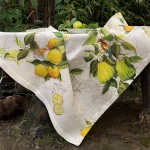 Tovaglia di lino con limoni Limoncello drappeggiata in giardino, con cedri, foglie verdi e fondo chiaro