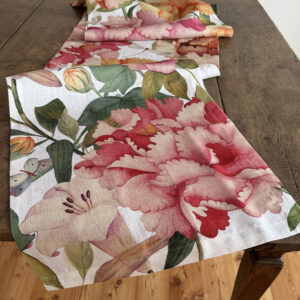 Runner di lino Peony su un tavolo di legno, con grandi peonie rosa e lampone, foglie verdi e una piccola farfalla.
